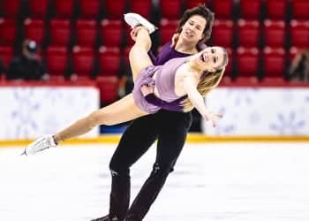 Wearing a violet-colored dress, Emilea Zingas is carried across the ice by Vadym Kolesnik, who is wearing all black.