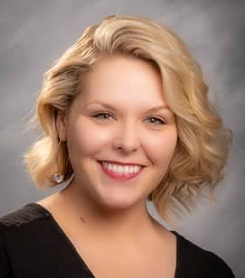 Headshot of a Caucasian woman smiling. She has shoulder length blonde hair and is wearing a black shirt